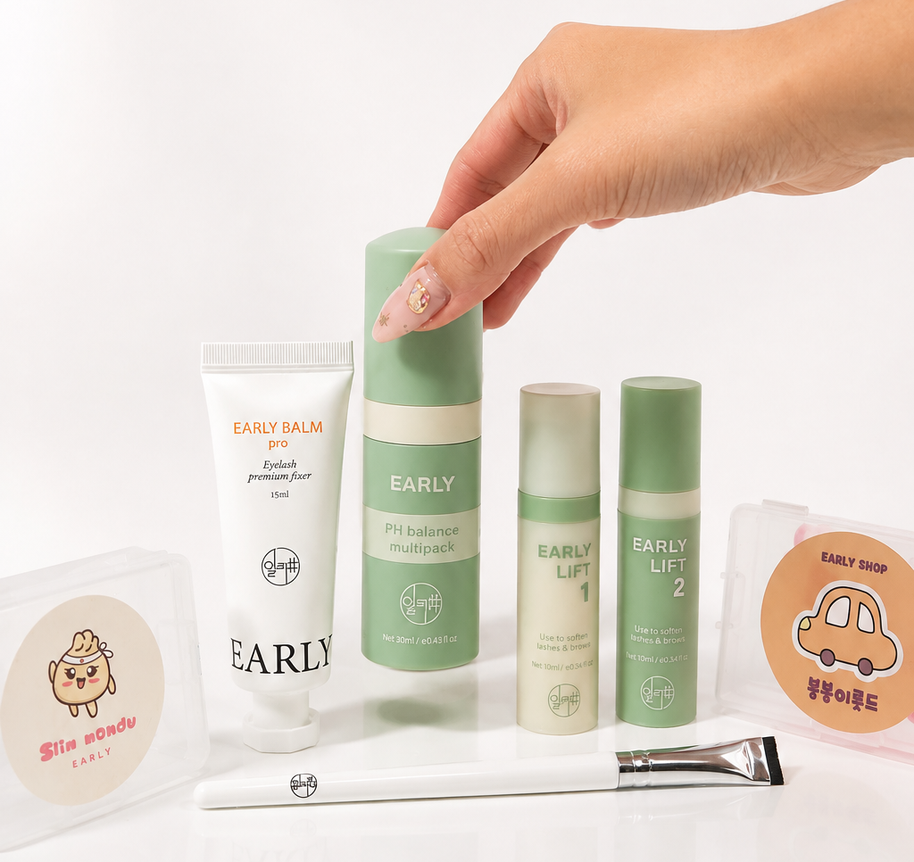 A hand with manicured nails reaches toward a green and white cosmetic product among a set of skincare items on a white surface against a white background. Visible products include an EARLY Balm tube, an EARLY LIFT serum bottle, two EARLY LIFT ampoules, a brush, and round packets labeled EARLY Balm and EARLY LIFT.